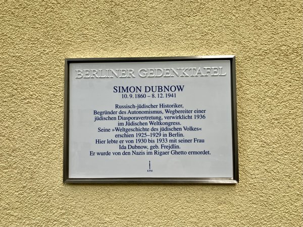 Gedenktafel für Simon Dubnow mit biografischen Angaben an einer gelben Wand