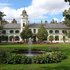 Britzer Schloss mit umliegendem Garten; im Vordergrund ein Springbrunnen und Pflanzen.