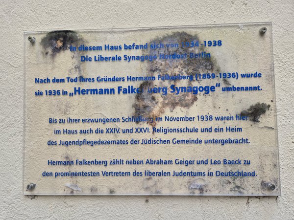 Gedenktafel aus Glas mit blauem Text zur Liberalen Synagoge. Die Tafel ist verschmutzt.
