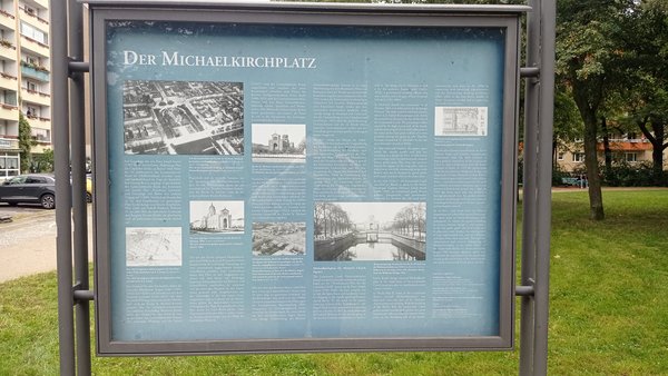 Blaue Informationstafel mit Text und Bildern zum Michaelkirchplatz.