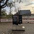 Die Tafel steht auf einem Sockel aus Stein am Pekinger Platz. Dahinter ein Gebäude und Bauzaun.