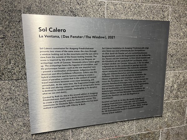 Metalltafel mit englischem Text zur Kunstinstallation 'Sol Calero La Ventana (Das Fenster / The Window), 2021', die zwei Ausblicke auf Berge und das Meer zeigt und kulturelle Einflüsse thematisiert