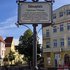 Das Schild steht auf einem Platz, dahinter Häuser und blauer Himmel.