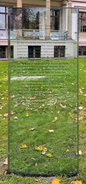 Eine Stele aus Glas mit Informationen zu Clara Israel, dahinter Rasen und das Standesamt Charlottenburg.