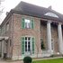 Zweistöckige Villa mit Säulen am Eingang, grünen Fensterläden und Efeu an der Fassade, im Hintergrund ein See und kahle Bäume
