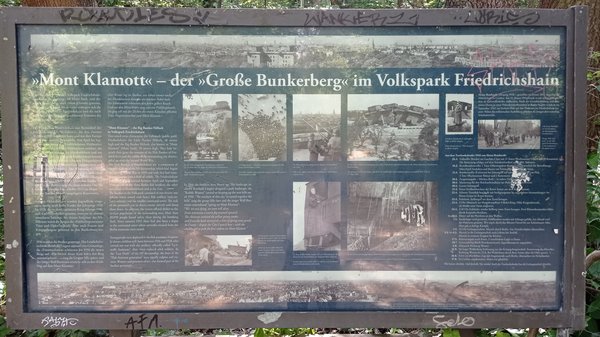 Informationstafel mit historischen Fotos und Texten zum Großen Bunkerberg Mont Klamott im Volkspark Friedrichshain, umgeben von Graffiti