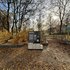 Infotafel mit Text und Bildern auf einem mit Herbstlaub bedeckten Weg in einem Park mit kahlen Bäumen und Steinmauern im Hintergrund