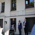 Drei Personen in formeller Kleidung enthüllen eine mit einem lila Tuch bedeckte Gedenktafel an einer Hausfassade, während mehrere Menschen Fotos machen