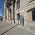 Fassade eines historischen Gebäudes mit Säulen und einer Geschichtstafel auf dem Bürgersteig
