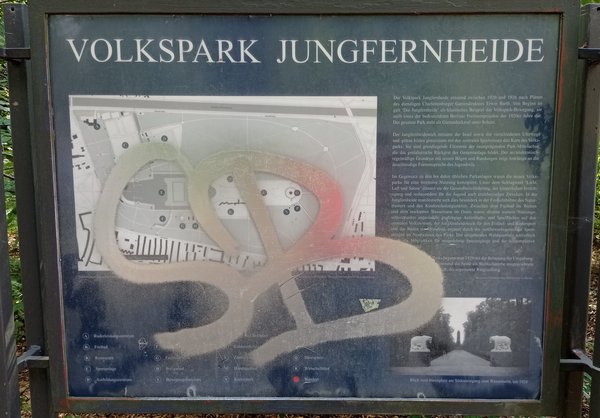 Blaue Infotafel mit Text, einem Lageplan und historischem Foto zum Volkspark. Die Tafel ist mit Graffiti beschriftet.