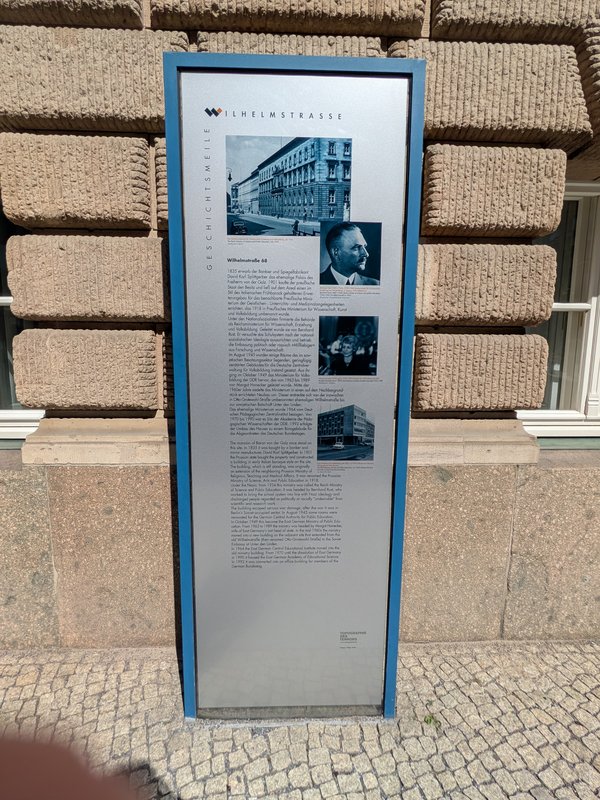 Informationstafel zur Geschichte der Wilhelmstraße mit mehreren historischen Fotos und Texten vor einem Sandsteinbau
