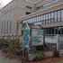 Gebäude mit großen Fenstern und einem mit Graffiti besprühten Informationsschild davor in einem verwilderten Innenhof