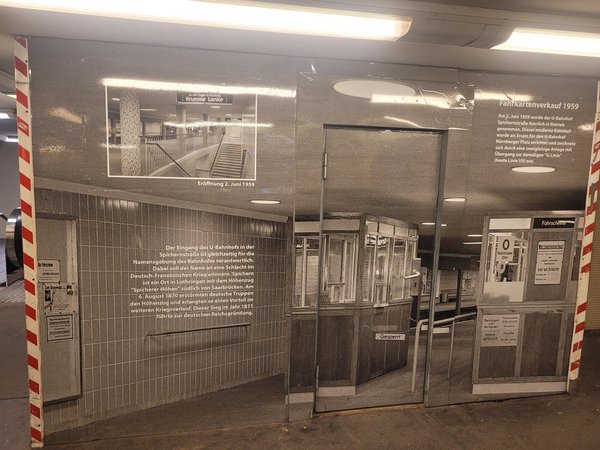 Schwarz-weiße Fotografie einer U-Bahn-Station mit Fahrkartenschalter und Informationstexten an der Wand.