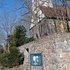 Kirchturm mit Fachwerk und rotem Dach hinter einer hohen Mauer aus unregelmäßigen Steinen und einem Informationsschild davor