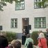 Ulrike Lauber hält die Laudatio vor einem Hauseingang, Menschen stehen davor.