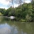 Parkteich mit Springbrunnen und von Bäumen umgebener Uferpromenade unter blauem Himmel