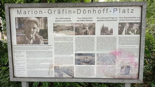 Informationstafel mit Text und historischen Fotos zum Marion-Gräfin-Dönhoff-Platz, darunter Porträt einer älteren Frau und mehrere schwarz-weiße Abbildungen von Gebäuden und Menschen.